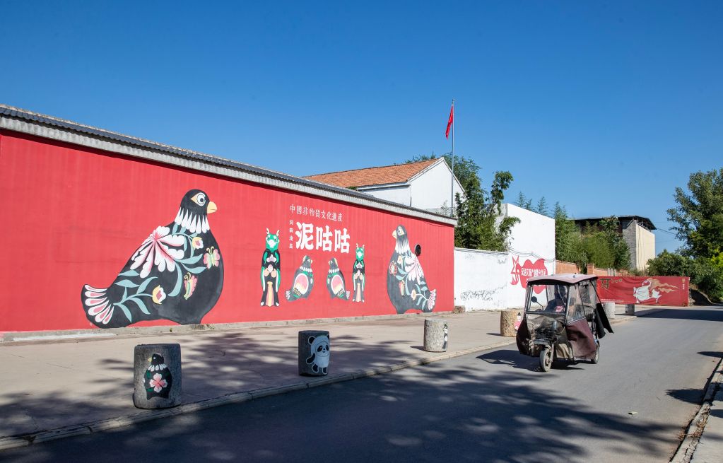 9月10日，在河南省浚县西杨玘屯村，村民从泥咕咕彩绘墙旁经过。新华社记者张帆 摄