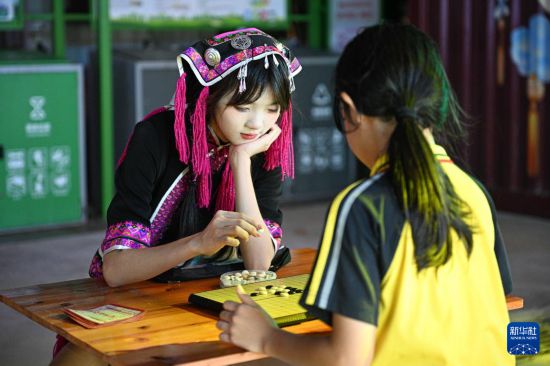 5月28日，在海南保亭七仙奇梦不夜城，演员（左）与游客下五子棋互动。